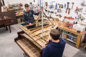 Tim and Dennis Chupp setting the plate into a Kurtzmann Grand Piano - Restoring Fine Pianos @ Chupp's Piano Service, Inc.